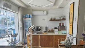 A modern kitchen with wooden bar counters, a dining area with chairs, and a view of the street through large windows.