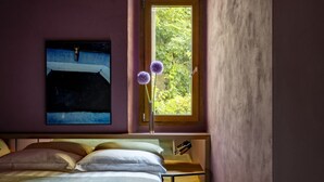 Un dormitorio con una cama, un ventanal con vistas a zonas verdes y un cuadro en la pared.