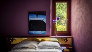 Un dormitorio con cama, ventana con vista a follaje y un cuadro en la pared.