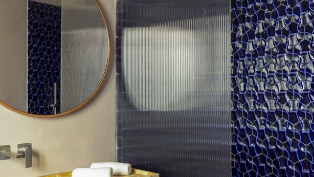 Un baño con lavamanos de mármol, un espejo y una pared con mosaico azul.