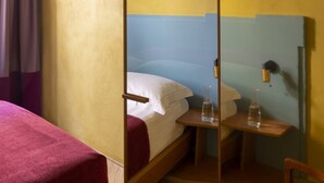 A single bed with a wooden frame, a bedside table with a water bottle, and a mirror on the wall. - The Wheels Florence Bed&Breakfast: Standard Bedroom OCRA (Florence)