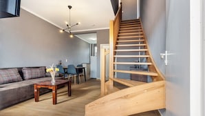 Een moderne woonkamer met een houten trap, een bank met geruite kussens, een salontafel en een eethoek op de achtergrond.
