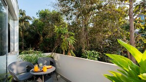 A balcony with wicker furniture, a table with a tray of orange juice, and lush greenery in the background. - 2BHK Apartment in North Goa , Reis Magos, Near Candolim (Verem)