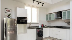 Une cuisine moderne équipée d’appareils électroménagers en acier inoxydable, d’un lave-linge et d’une fenêtre laissant entrer la lumière naturelle.