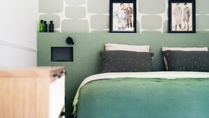 A bedroom with a green bedspread, two pillows with gold patterns, and two framed pictures on the wall. - Villa Nady (Pauillac)