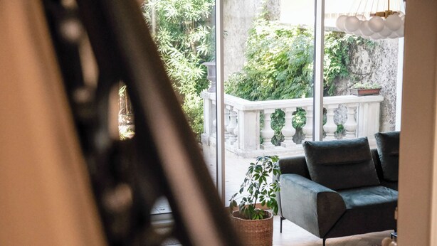A modern living room with a grey sofa, a large window, and a balcony with a white balustrade. - Villa Nady (Pauillac)