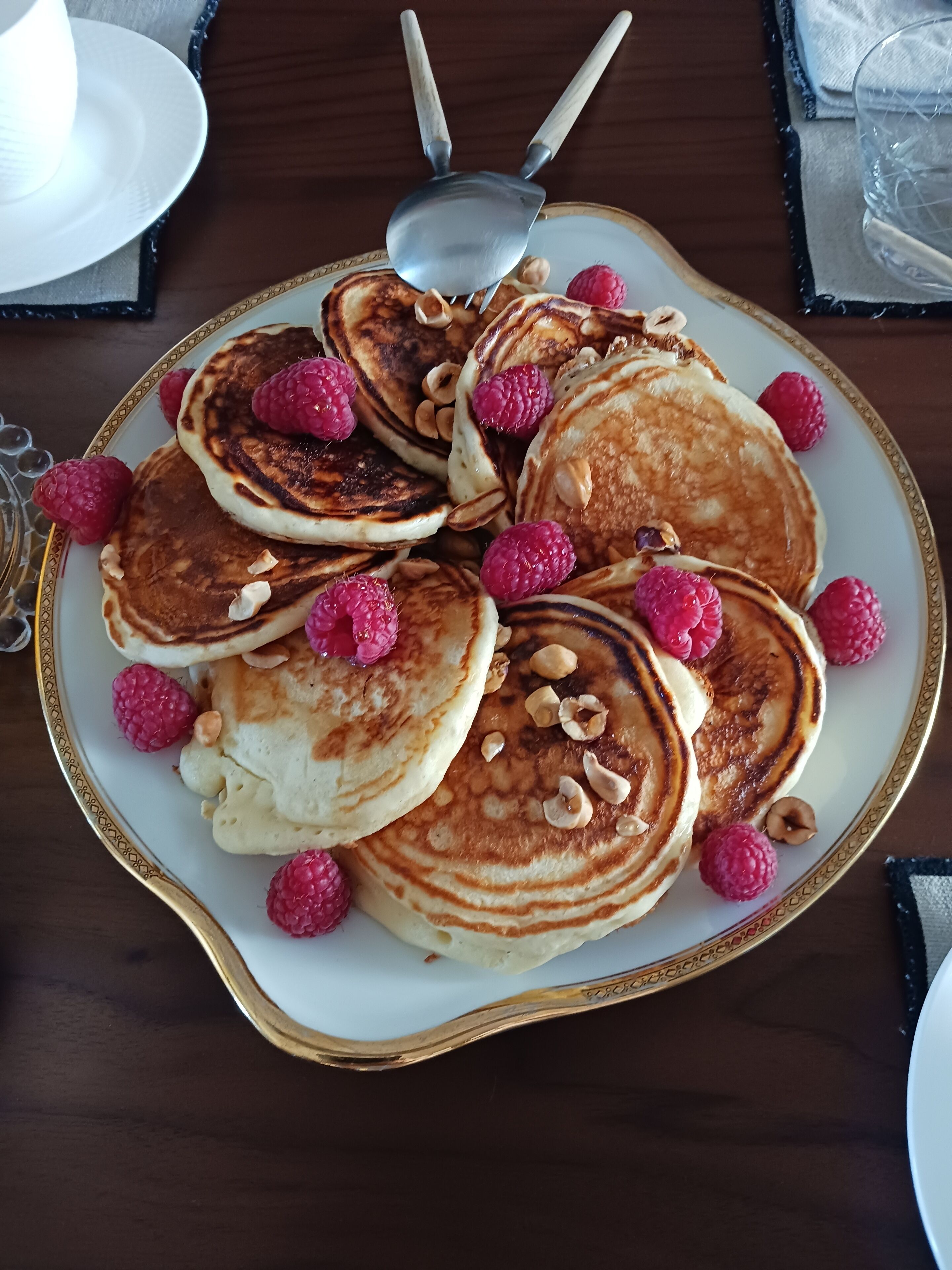 Un plato de panqueques con frambuesas y nueces sobre un plato blanco con borde dorado.