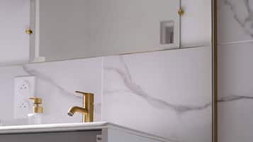 A modern bathroom with a white vanity, gold fixtures, and marble walls.