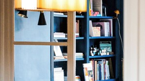 A room with a wooden table, a glass dome centerpiece, a blue bookshelf, and a lamp. - Villa Nady (Pauillac)