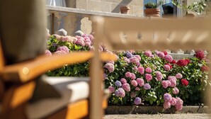 A stone building with a balcony, potted plants, and a wooden chair. - Villa Nady (Pauillac)