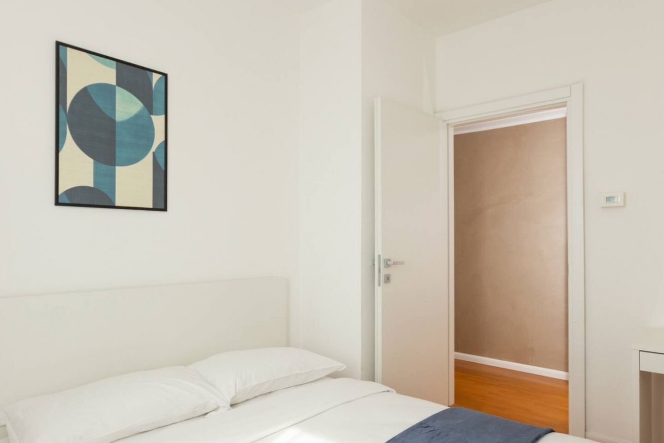 A bedroom with a bed, a white door, and a framed abstract painting on the wall.