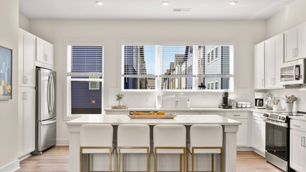 Une cuisine moderne avec des meubles blancs, un îlot central doté de tabourets de bar, des appareils en acier inoxydable et de grandes fenêtres offrant une vue sur la ville.