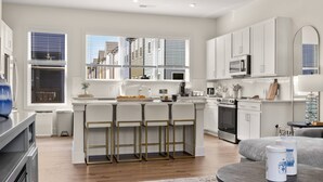 Une cuisine moderne avec des meubles blancs, un îlot central doté de tabourets, un four à micro-ondes et une cuisinière.