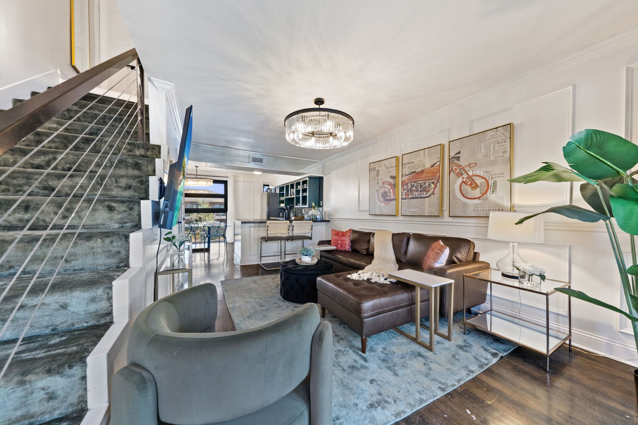 A spacious living room with a large staircase, a chandelier, and a dining area.