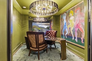 A hallway with a chandelier, a painting, and a dining area with chairs and a table.