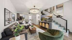 Un salon moderne avec un canapé, une table basse et une plante. On y trouve un escalier avec une rampe et un tableau accroché au mur.