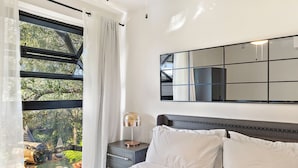 A bedroom with a large window, a bedside table with a lamp, and a bed with white bedding. - Second-floor bright & airy 2-story loft in Dallas’ Historic Munger District featuring luxury linens, a fully equipped kitchen, spacious living area, and access to an award-winning courtyard retreat—ideal for extended stays or weekend getaways. (Dallas)