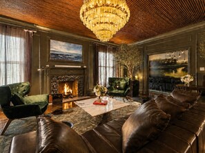 A room with a fireplace, leather sofas, a chandelier, and artwork on the walls.