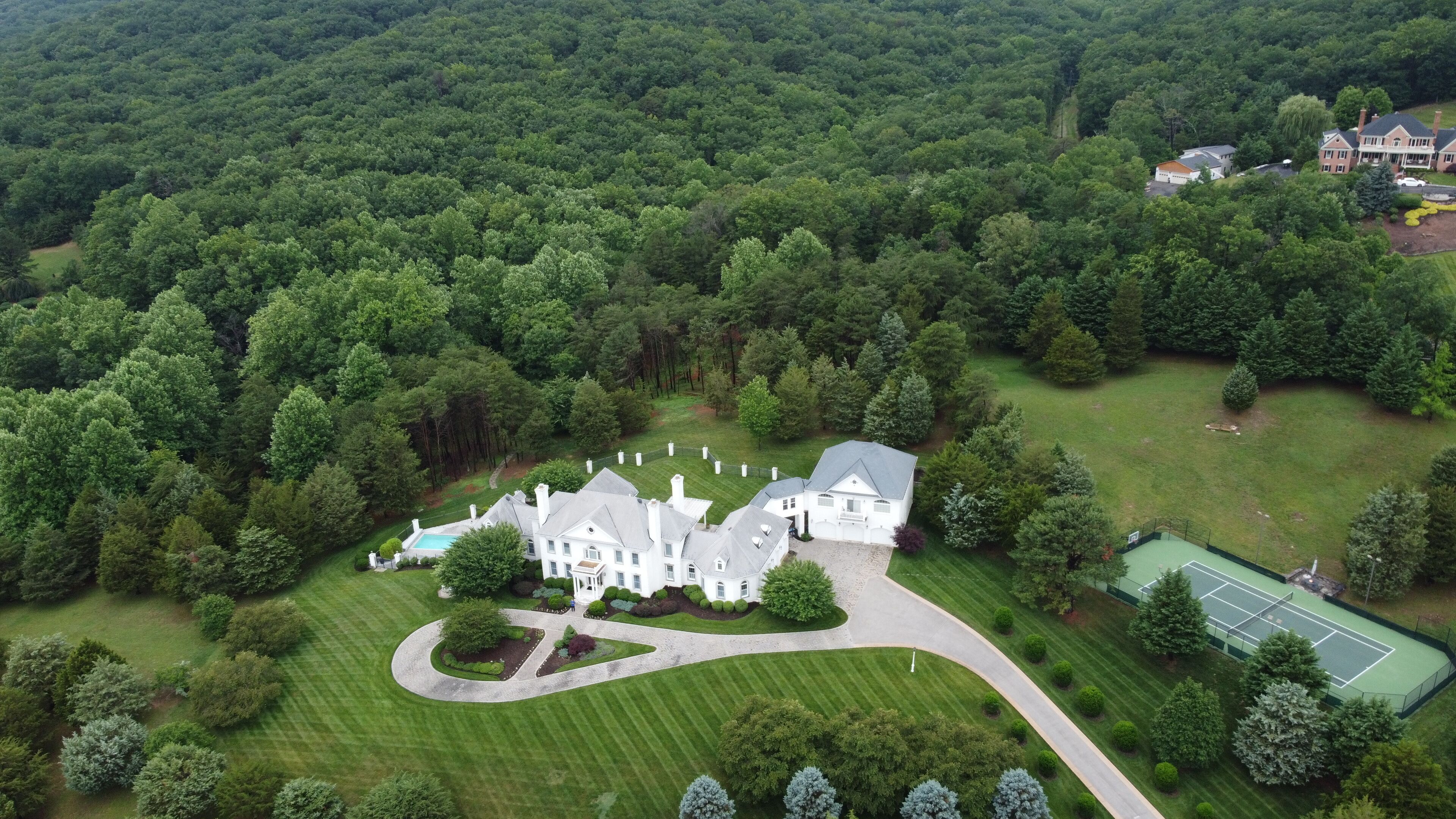 An aerial view of a large estate with multiple buildings, a tennis court, and a well-maintained lawn.