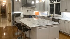 A modern kitchen with white cabinetry, a large island, stainless steel appliances, and pendant lighting. - Harmony Hall at The Grange, Luxury Estate in Virginia Wine Country (Haymarket)