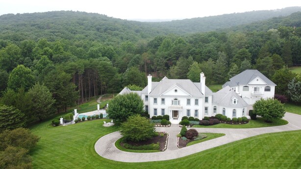 A large, white, two-story house with a well-maintained lawn and a winding driveway. - Harmony Hall at The Grange, Luxury Estate in Virginia Wine Country (Haymarket)