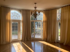 A spacious room with large windows, a chandelier, and a view of a garden.