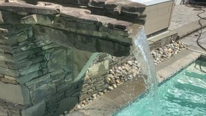 A pool with a waterfall feature, surrounded by stone walls and a stone ledge. - Harmony Hall at The Grange, Luxury Estate in Virginia Wine Country (Haymarket)