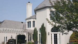 A white two-story house with a covered patio, a chimney, and a garden with a fountain. - Harmony Hall at The Grange, Luxury Estate in Virginia Wine Country (Haymarket)