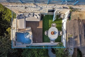 Vista aerea di un giardino sul retro con una vasca idromassaggio, un patio in legno e un'area salotto con tavolo e sedie.