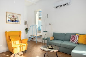 A living room with a yellow armchair, a blue staircase, a green sofa, and a small table with a book.