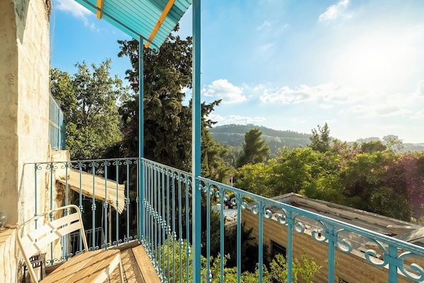 A balcony with a view of a hilly landscape, a wooden deck, and a metal railing.