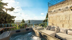 A hot tub with a view of mountains, a stone wall, and a seating area with cushions. - Timeless Charm, Stunning Views & Serene Comfort (Jerusalem)