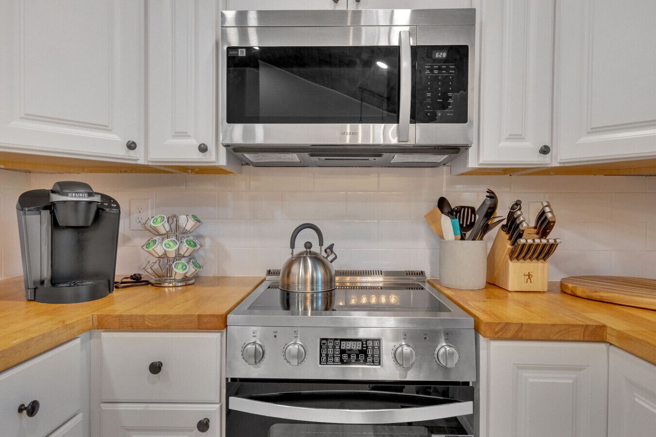 A modern kitchen with a stainless steel microwave, coffee maker, kettle, and oven.