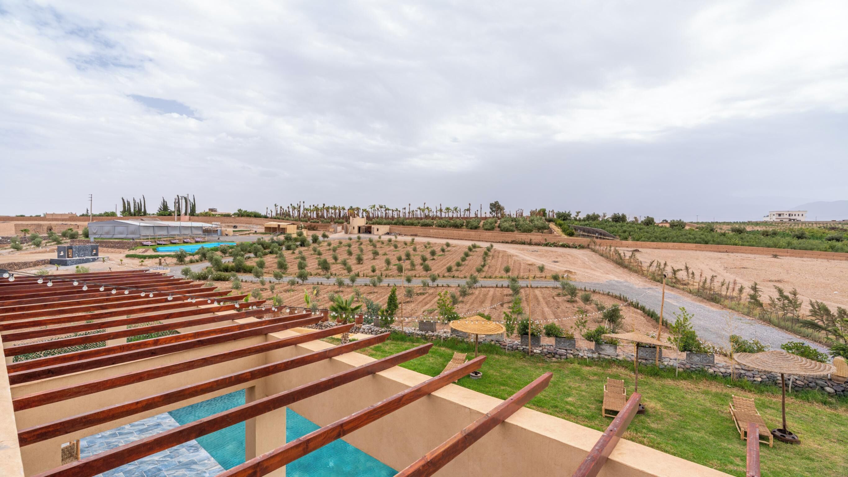 A pool area with wooden deck railings, a landscaped garden with various plants, and a distant view of a residential area.