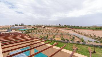 A pool area with wooden deck railings, a landscaped garden with various plants, and a distant view of a residential area.