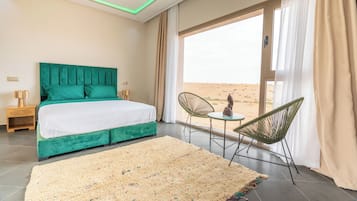 A bedroom with a bed, a view of the desert, and a small table with chairs.