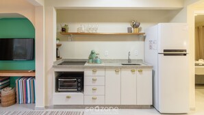 Una cocina moderna con armarios blancos, horno integrado, refrigerador y repisa de madera sobre el lavamanos.