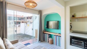 Una sala de estar moderna con un sofá, una televisión, una zona de cocina con un tostador y vistas a un edificio.