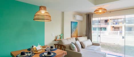 A modern living room with a dining area, a sofa, and a large window offering a view of the outside.