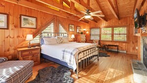 Ein Schlafzimmer einer Holzhütte mit Bett, Bank, Kamin und Deckenventilator.