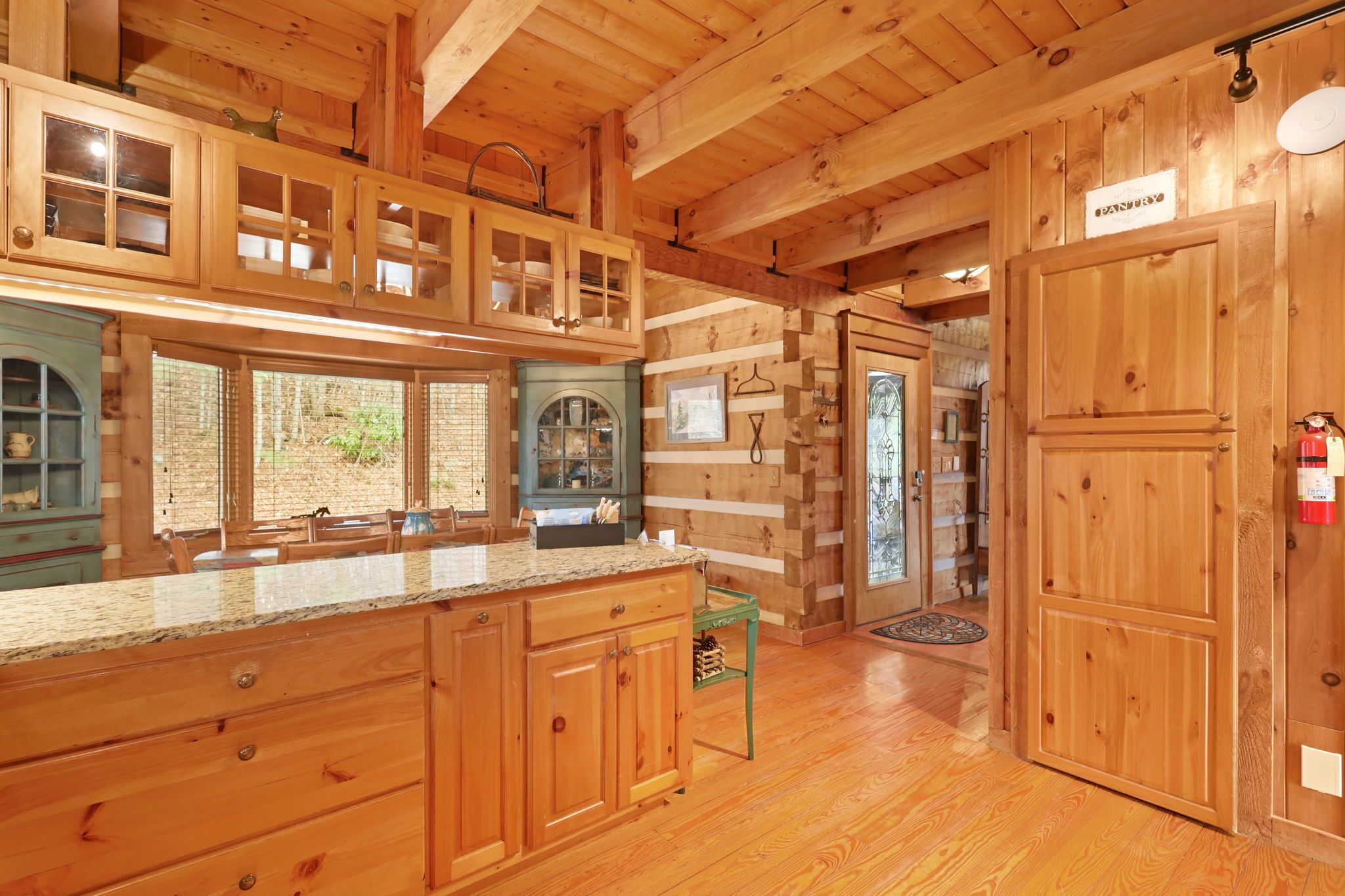 A wooden cabin interior with a kitchen featuring a granite countertop, wooden cabinets, and a window overlooking a brick wall.