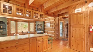 Ein Holzblockhaus-Interieur mit einer Küche, die eine Granit-Arbeitsplatte, Holzschränke und ein Fenster mit Blick auf eine Backsteinmauer zeigt.