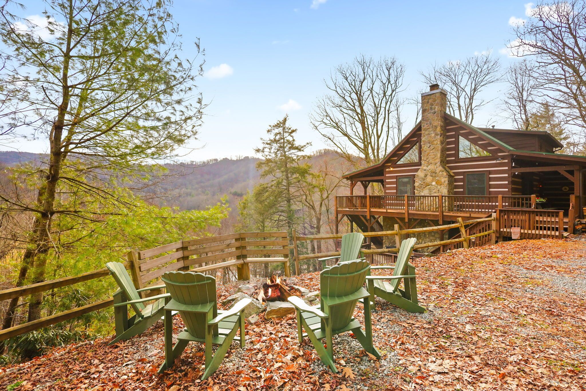 A cabin with a stone chimney, wooden deck, and green Adirondack chairs.