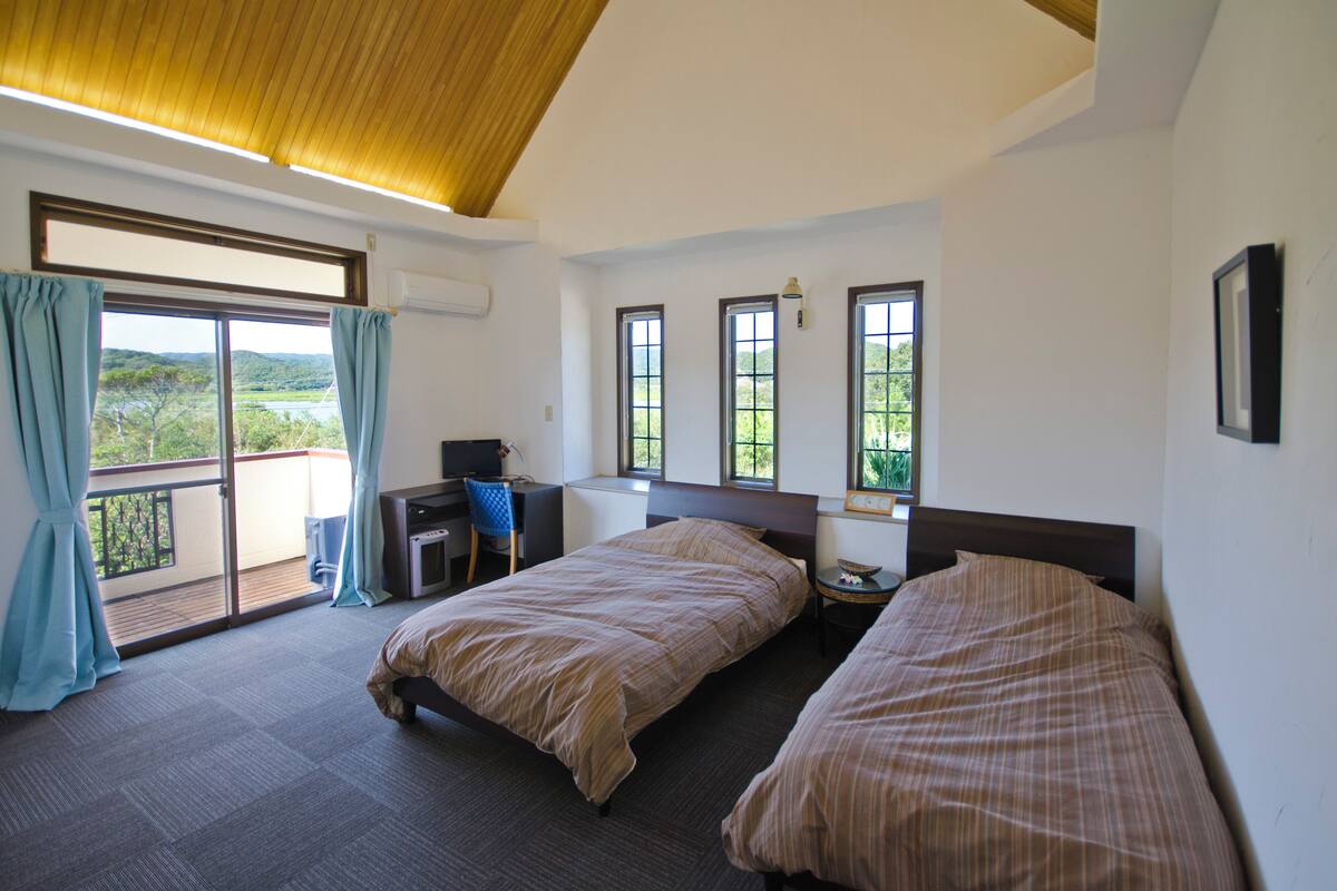 Una habitación de hotel con dos camas, un escritorio y un balcón con vistas al campo.