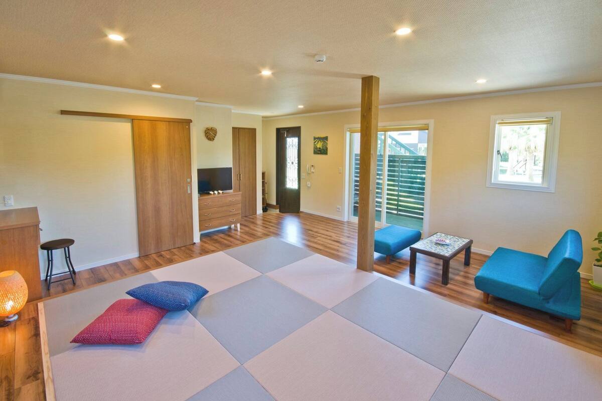 Amplia sala de estar con esteras de tatami, un sofá azul, una mesita y un armario de madera.