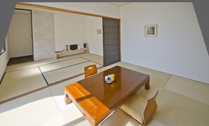 Ein traditioneller japanischer Raum mit Tatami-Böden, einem Holztisch mit Kissen und einer Schiebetür.