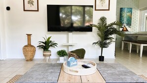 A living room with a large flat-screen TV mounted on the wall, a coffee table with a tray, and several potted plants. - The Oasis at Lake Eva (Haines City)
