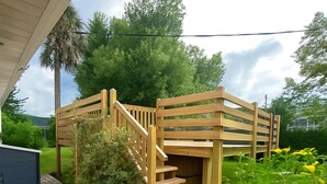 A wooden deck with a staircase leading to a covered area, surrounded by greenery and a small garden. - The Oasis at Lake Eva (Haines City)