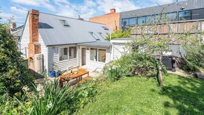 Propiedad residencial con una casa independiente que cuenta con una chimenea de ladrillo destacada, un porche cubierto y un jardín con diversas plantas.