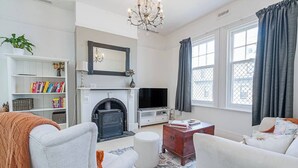 Una sala de estar con chimenea, televisor, estantería y un ventanal con cortinas.